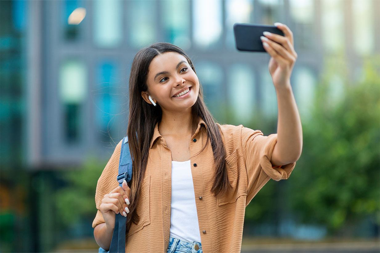 Estudiante internacional haciéndose un selfie en su nuevo campus, emocionada por comenzar su experiencia en el extranjero.